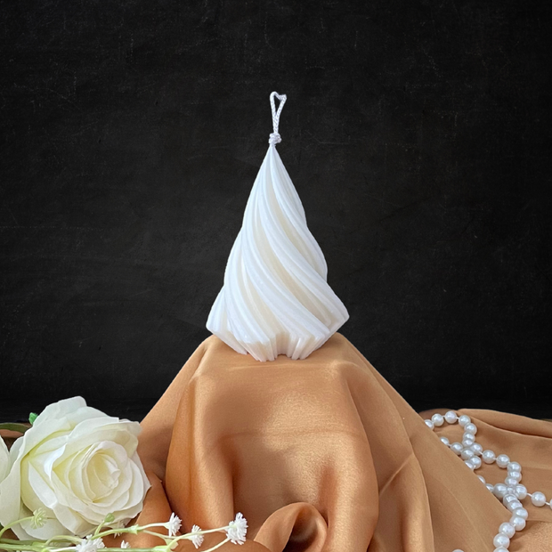 White twisted pillar candle from The Twirl Pillar Candle Collection displayed on beige satin cloth with white roses and pearl necklace.