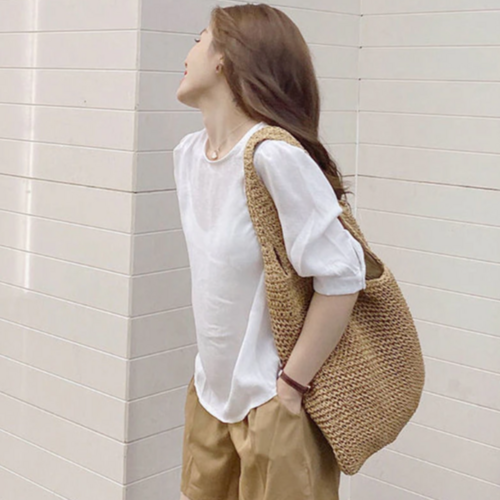 Woman wearing a casual summer shoulder beach bag made of straw with a white blouse and beige shorts