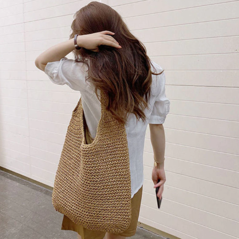 Woman carrying a casual summer shoulder beach bag made of woven straw with a soft, bohemian style design.