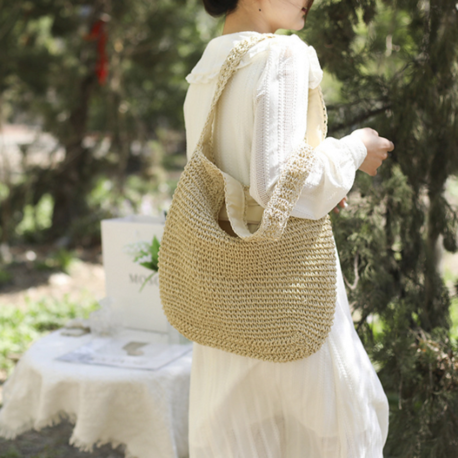 Casual summer shoulder beach bag made of straw with roomy interior and bohemian style worn by woman outdoors