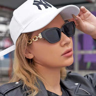 Fashion Cat Eye Sunglasses with black frame and gold chain detail worn with white cap and leather jacket