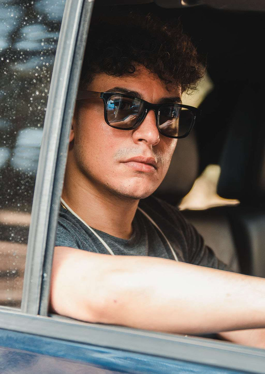 Man wearing Eyewood ReInvented square acetate and walnut wood sunglasses with black polarized lenses in a car