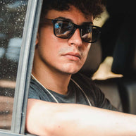 Man wearing Eyewood ReInvented square acetate and walnut wood sunglasses with black polarized lenses in a car