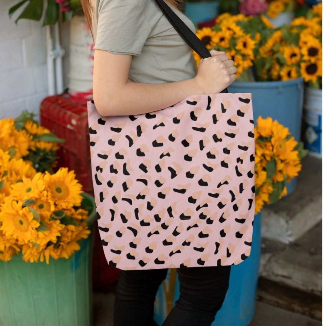 Medium pink leopard print shopper tote bag with black handles, worn by person, surrounded by sunflowers