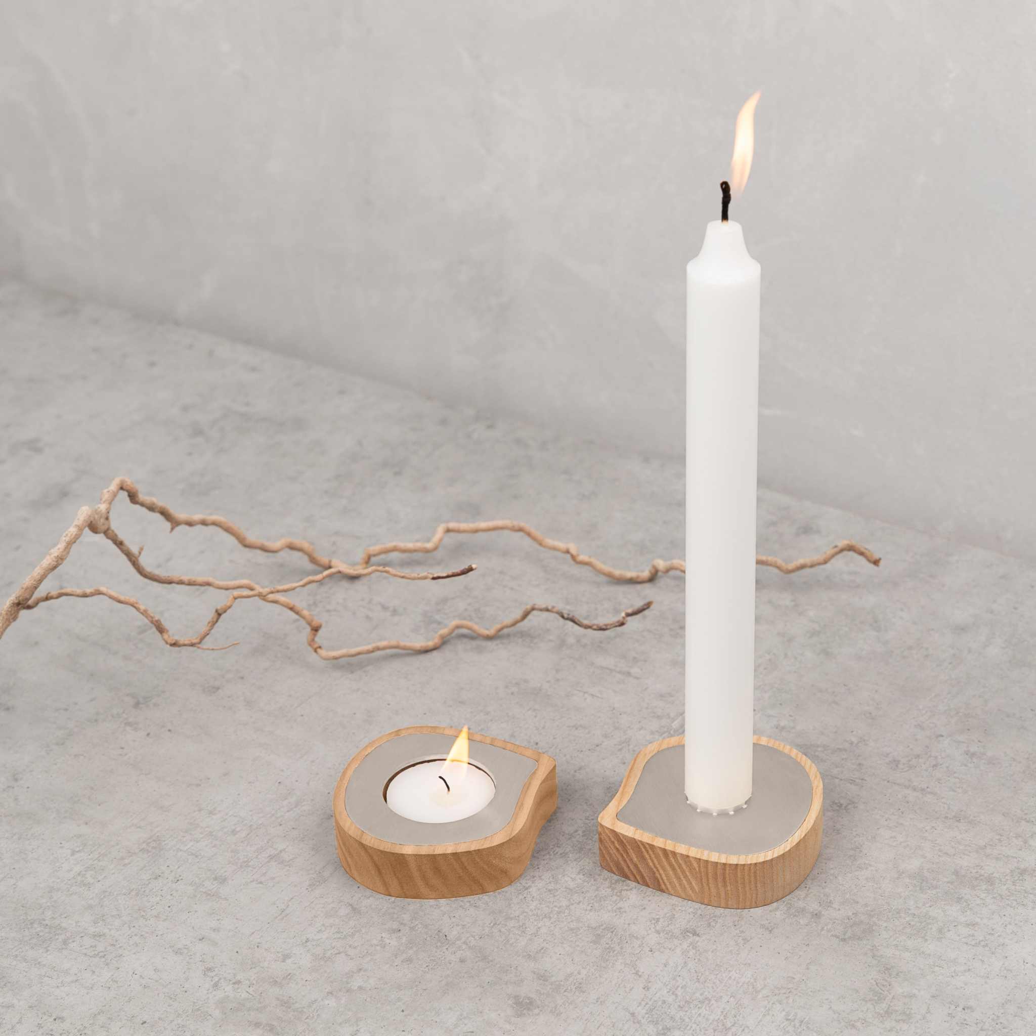 Ash wood taper candle holder and tealight holder with stainless steel detail on concrete surface