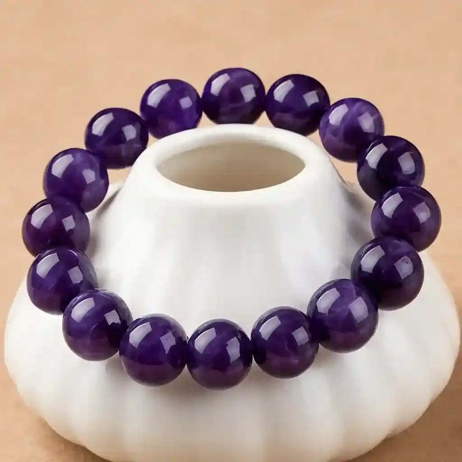 Dark purple gem stretch bracelet with round beads on elastic cord displayed on white ceramic holder