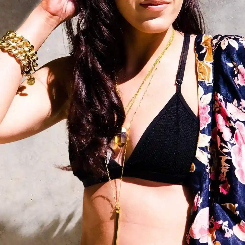 Glow Crystal Quartz Necklace with gold-plated chain and genuine crystal quartz pendant worn layered with black top and floral cover-up