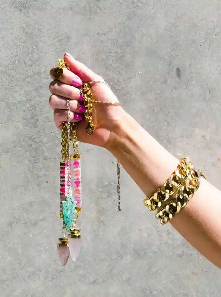 Hand holding St. Tropez Blue Quartz Necklace with colorful bead strap and 24K gold-plated chain against gray background