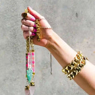 Hand holding St. Tropez Blue Quartz Necklace with colorful bead strap and 24K gold-plated chain against gray background