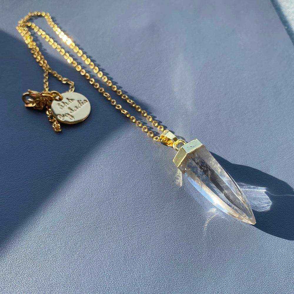 Glow Crystal Quartz Necklace with gold-plated chain and clear crystal quartz pendant on dark surface