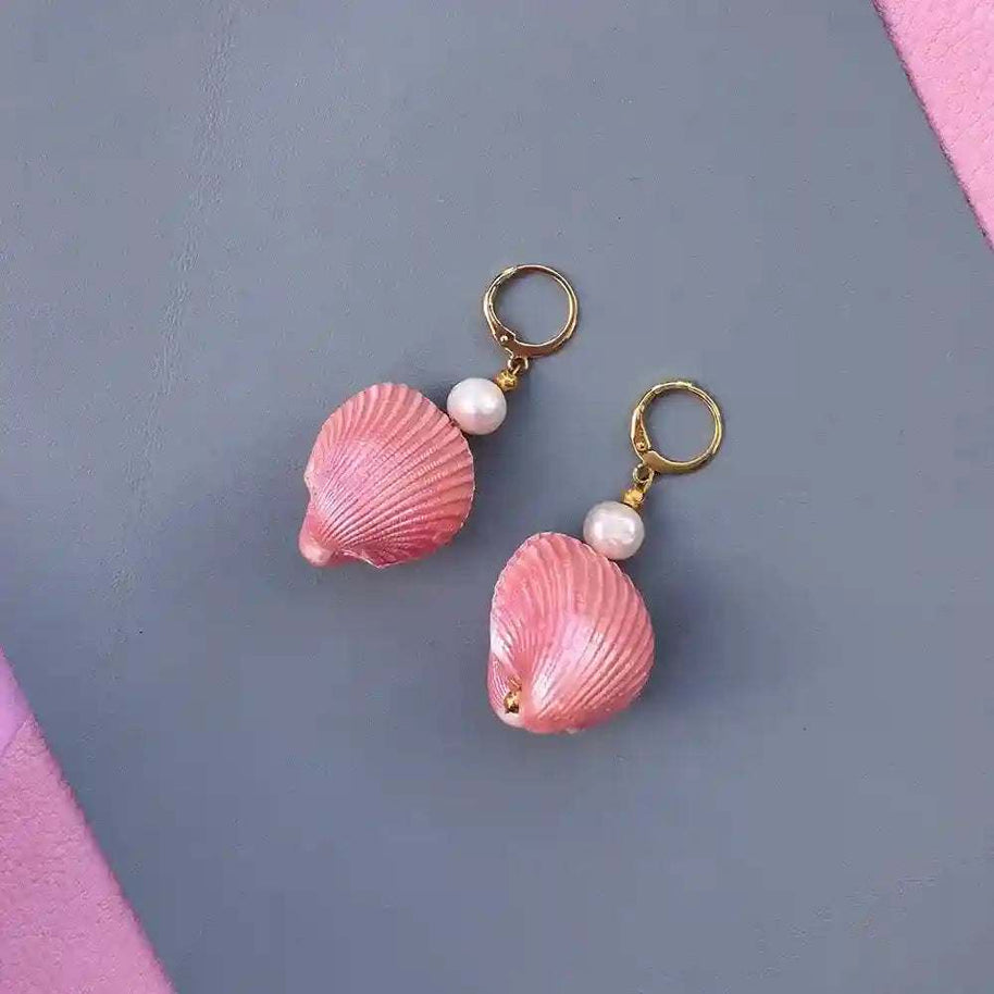 Pair of Candy Shell Pearl Earrings with pink clamshells, freshwater-style pearls, and 24K gold-plated hoops on a gray and pink background