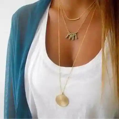 Turquoise layered necklace with gold chains and pendants styled over white top and blue outerwear