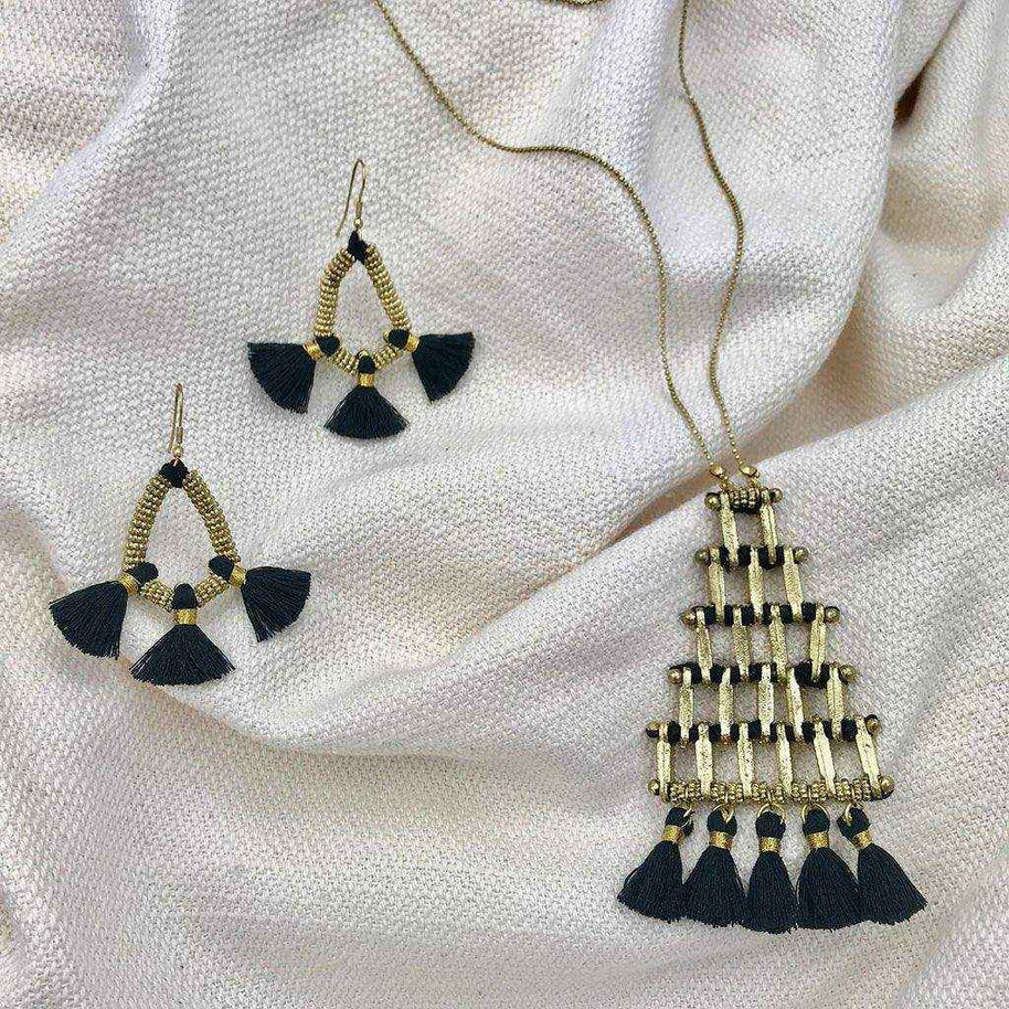 Kai Pyramid Tassel Necklace with black tassels and matching earrings on beige fabric background