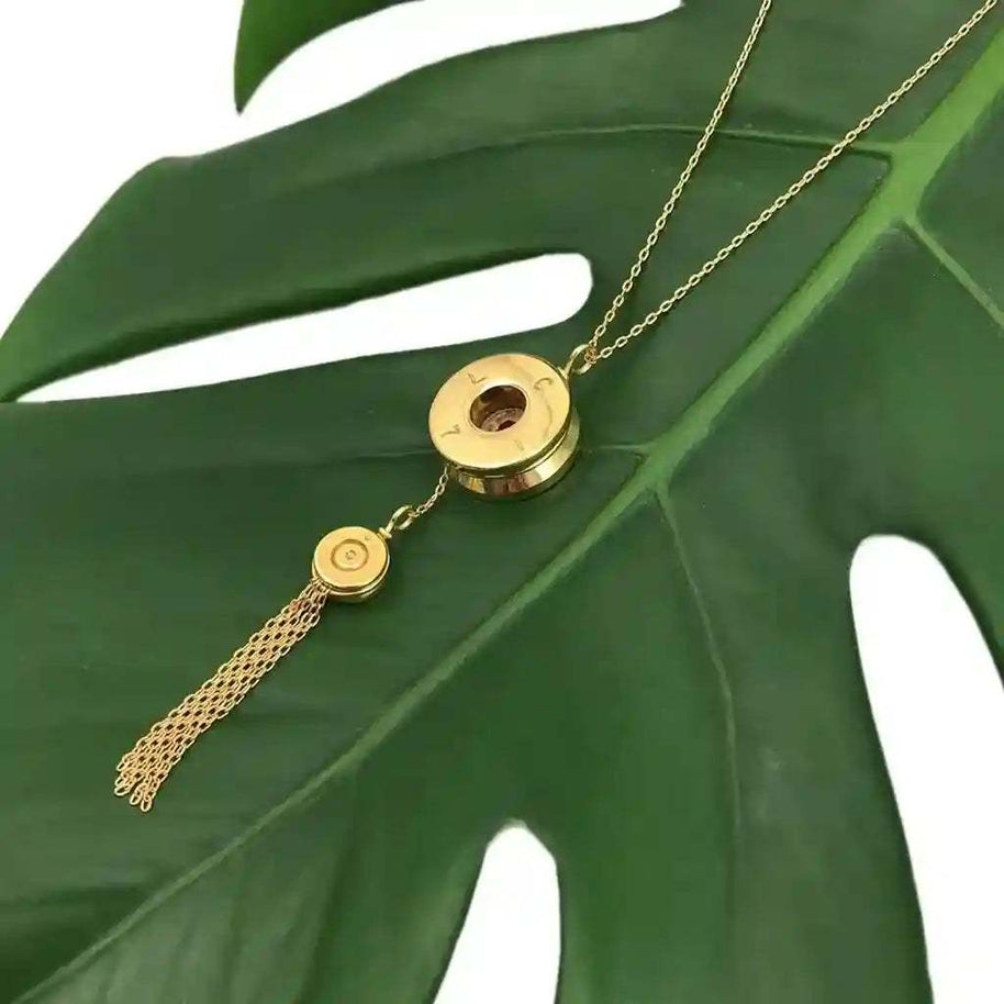 Gold plated Bullet Tassel Necklace with recycled bomb shell pendant and bullet fragment detail on green leaf background